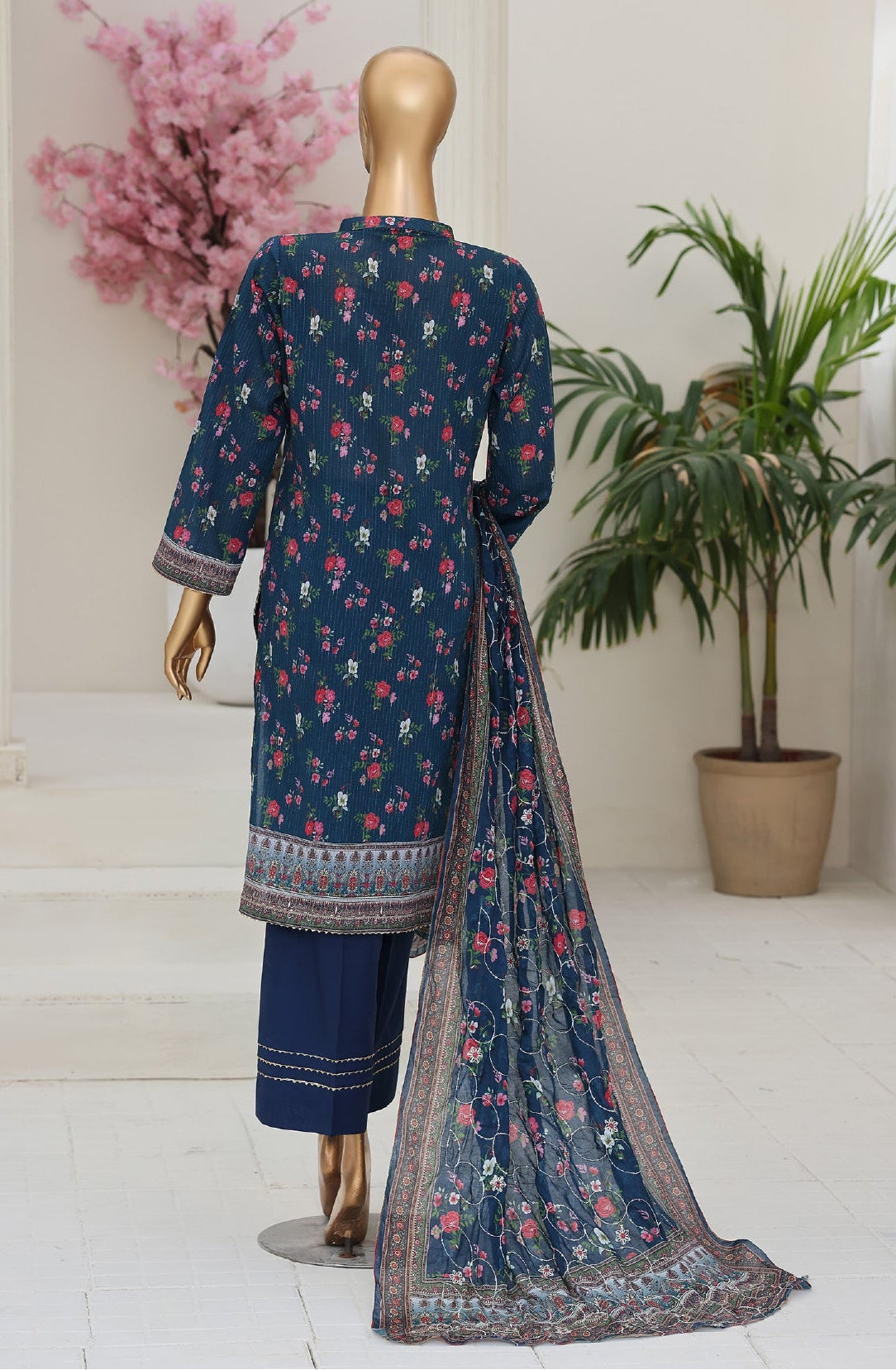 Navy blue traditional outfit with floral patterns on a mannequin against a white background with plants.